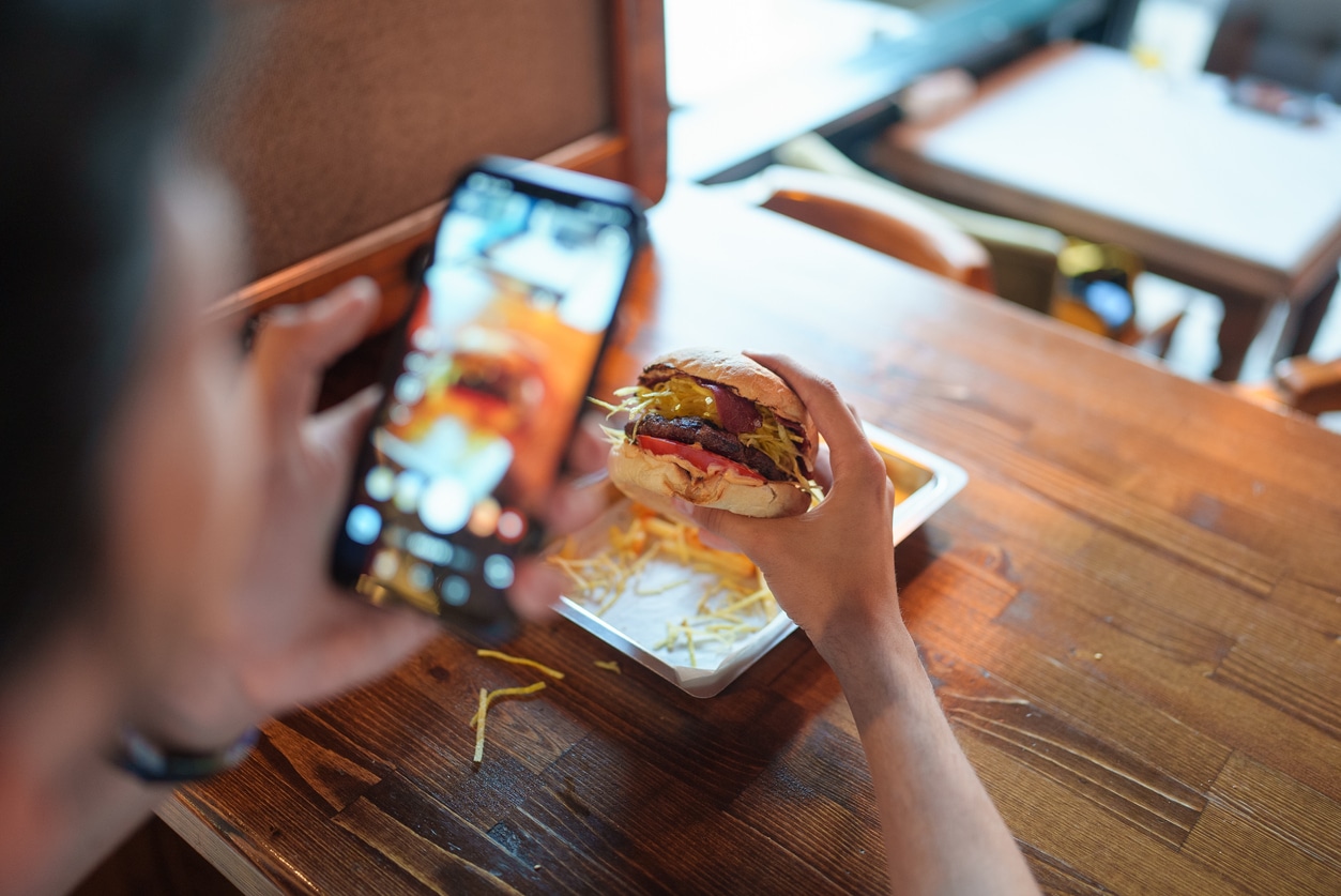 Young man is taking a photo of his burger with his phone