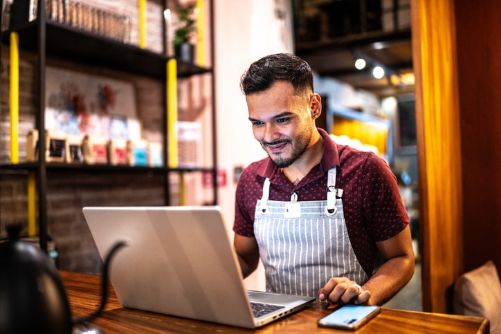 Small business owner young man using laptop at a coffee shop